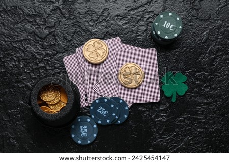 Poker chips, cards, pot with coins and lucky clover on black grunge background. St. Patrick's Day celebration