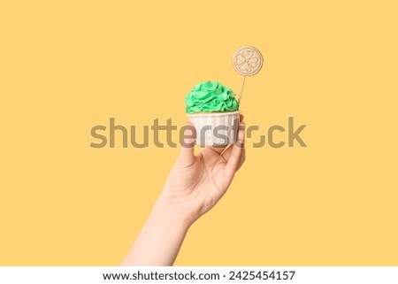 Female hand with tasty cupcake for St. Patrick's Day on beige background
