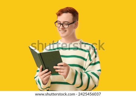 ?Young man in eyeglasses reading book on yellow background