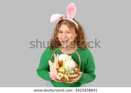 Beautiful young happy woman in bunny ears with Easter basket on grey background
