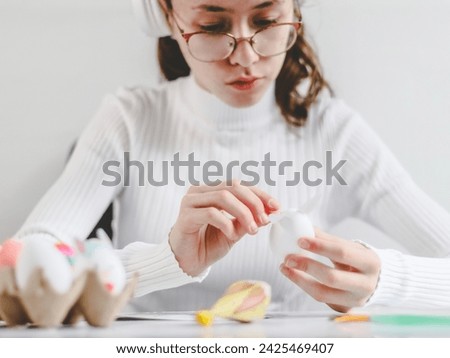 Beautiful caucasian teenage girl in a white turtleneck with glasses enthusiastically pasting stickers with bunny ears