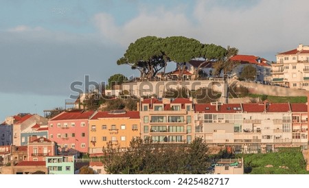 Famous viewpoint Miradouro da Senhora do Monte with city view of Lisbon timelapse during sunset with colorful houses around, Lisbon, Portugal. Clouds on the sky over green trees Royalty-Free Stock Photo #2425482717