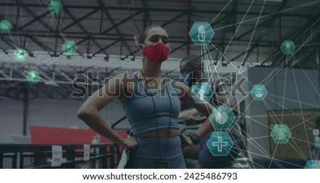 Globe of medical icons spinning against female fitness trainer wearing face mask standing in the gym. medical research and and fitness concept