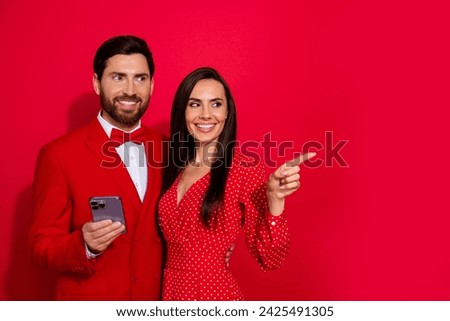 Photo of two attractive elegant lovers embrace hold smart phone look direct finger empty space isolated on red color background