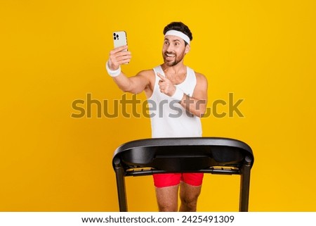 Photo of funny excited guy activewear walking treadmill showing finger apple iphone samsung modern gadget isolated yellow color background