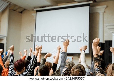 A group of people with their hands raised, eager to participate in a meeting or class, with a blank screen in the background. Suitable for stock photography and advertising.