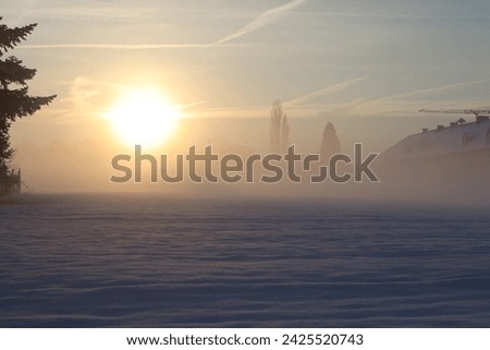 A sunrise during a cold winter morning with snow and mist, a farm and trees barely visible.