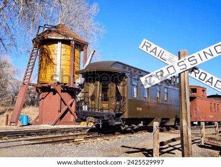 An Old Wooden Passenger Car and Caboose Stopped at a Railroad Crossing Near a Water Tower Royalty-Free Stock Photo #2425529997