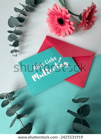A photo featuring a blue envelope placed alongside a red envelope, creating a vibrant and colorful composition. Text Alles Liebe zum Muttertag means All Love on Mother's day.