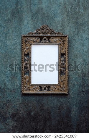 Vintage openwork bronze metal frame on a blue and green old wall with drips, texture background, empty picture frame mockup