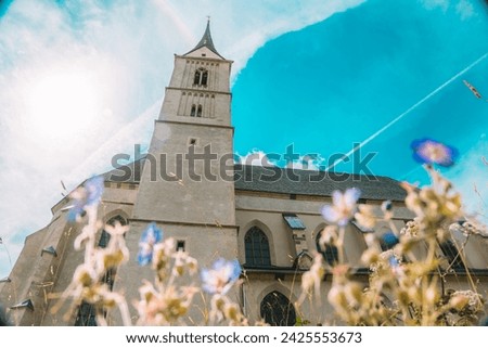 Church of St. Leonard and meadow flowers on blue sky background.Catholic Church architecture outside.Christian and catholic faith symbol.Religious symbol.Church building in Gothic style on blue sky