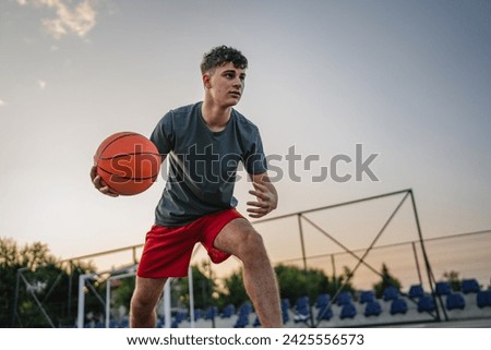 One teenager caucasian male caucasian young man stand on basketball court with ball in the evening ready to play game copy space real person