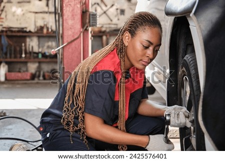 One African American female automotive mechanic worker screws car wheel nuts with wrench for repair at garage, professional labor works, vehicle maintenance service jobs, industry occupation business.