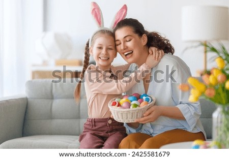 Happy holiday! Mother and her daughter with painting eggs. Family celebrating Easter. Cute little child girl is wearing bunny ears.