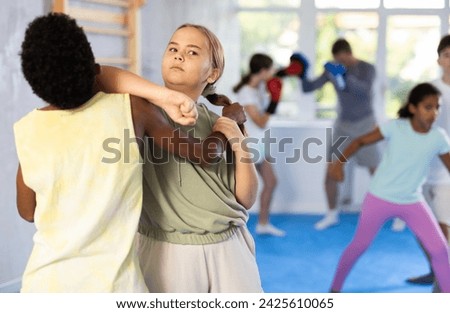 Focused preteen girl practicing self-defense moves in mock bout with black boy, gripping opponent arm and delivering elbow strike to chin