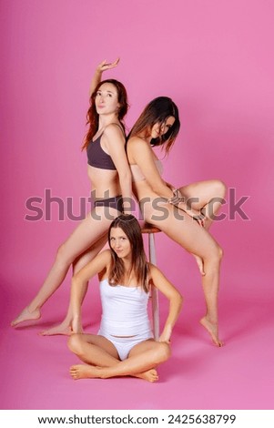Trio of young women in simple undergarments display creativity with dynamic poses against a vivid pink background in a photo studio.  Royalty-Free Stock Photo #2425638799