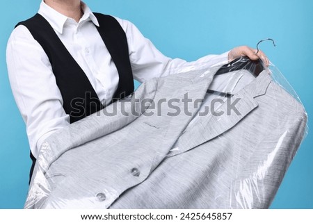 Dry-cleaning service. Woman holding jacket in plastic bag on light blue background, closeup Royalty-Free Stock Photo #2425645857