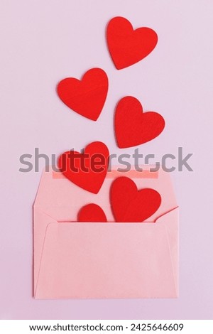 Valentines day theme background with pink envelope and red wooden hearts on a pink background, copy space