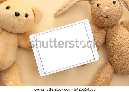 Modern tablet and stuffed animals on beige background, flat lay. Space for text