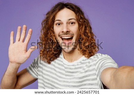 Close up young man wears grey striped t-shirt casual clothes doing selfie shot pov on mobile cell phone waving hand isolated on plain pastel light purple background studio portrait. Lifestyle concept