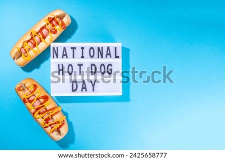 National Hot Dogs day background, hotdog summer party festival foods, Two tasty classic american hot dogs with sauces and lightbox sign with inscription National Hot Dog Day on blue background 