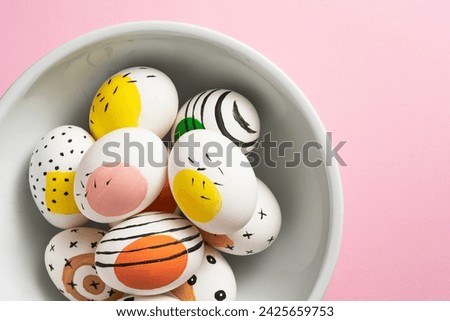 Colourfully painted easter eggs in white ceramic bowl on pink background
