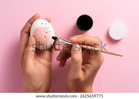Hands painting pink easter egg on pink background