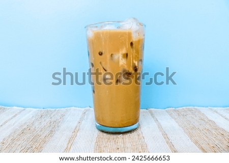 Iced mocha coffee in a tall glass full of ice isolated on blue background. Fresh mocha iced coffee