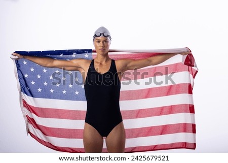 Female swimmer in a swimsuit holds an American flag. Pride and patriotism emanate from the female swimmer's confident pose. Royalty-Free Stock Photo #2425679521