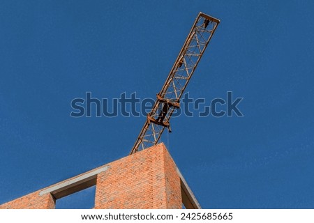 It's view of incomplete red brick house without roof. It is a close up view of an unfinished apartment building. Its sunny day. It's photo of tower crane.