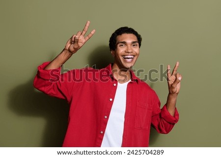 Photo of cool funky guy wear red shirt showing two v-signs smiling isolated khaki color background