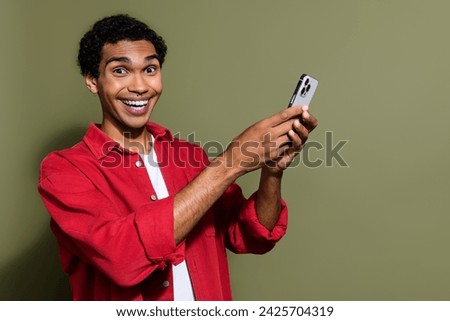 Photo of cheerful good mood guy wear red shirt texting sms apple iphone samsung gadget empty space isolated khaki color background