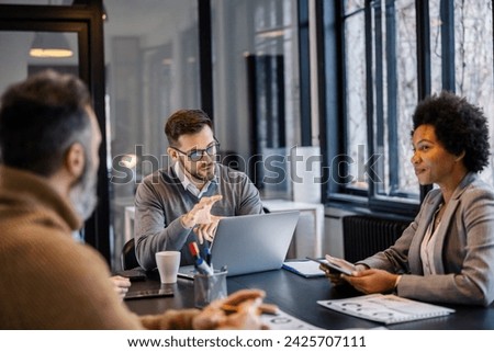 A serious team lead with laptop is discussing project with his interracial team at meeting room. Royalty-Free Stock Photo #2425707111