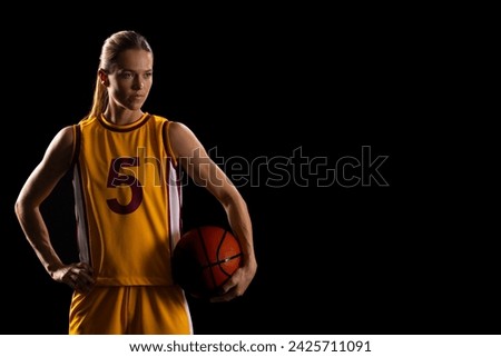 Young caucasian female basketball player poses in a basketball uniform on a black background, with copy space. Her stance and expression exude determination and athleticism on the court.
