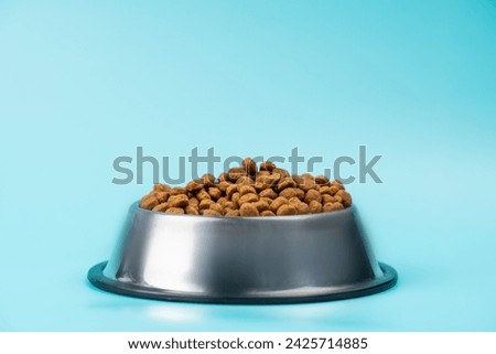 Brown cat or dog kibble in a metal bowl isolated top view close-up. Nutritious healthy diet pet food scattered around, falls and cascades the bowl. Dry cat or dog food spills from a bowl. Royalty-Free Stock Photo #2425714885
