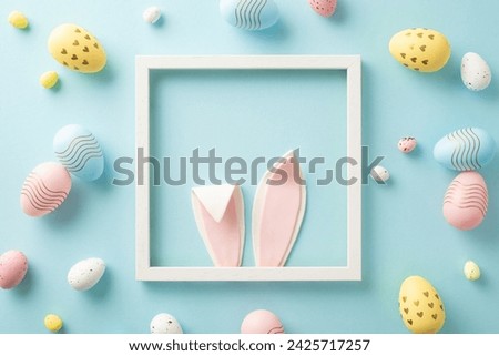 Whimsical Easter magic concept. Top view image featuring an endearing Easter bunny in a photo frame, peeking out with charming ears, alongside vibrant eggs on a baby blue surface