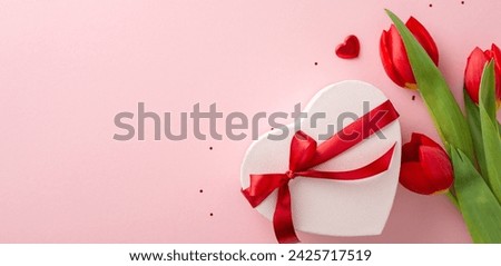 Prime feminine event concept. Top view picture of a gift in heart shape, adorned with bow, sparkle, small hearts, and fresh-cut tulips on a pastel pink plane, with area for text or marketing