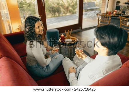 Two smiing diverse friends talking and drink wine during holiday party at home Royalty-Free Stock Photo #2425718425