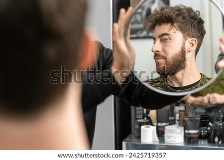 Young man adjusting his hairstyle in the mirror - Focused on personal grooming and style. Royalty-Free Stock Photo #2425719357