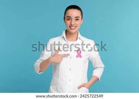 Mammologist pointing at pink ribbon on light blue background. Breast cancer awareness