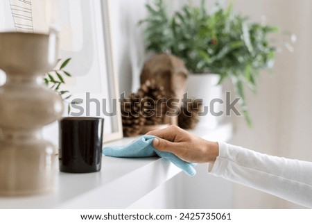 Cropped shot of woman hand hold wet cloth and remove dust from shelf at home. Female housewife wipe furniture in living room with microfiber rag. Cleaning and household chores concept