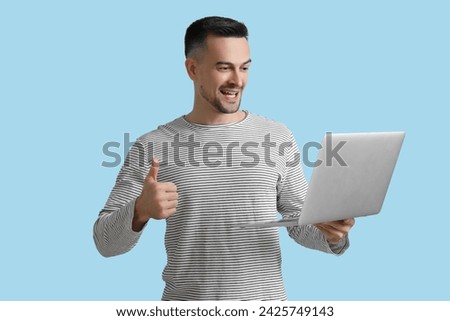 Happy young man with laptop showing thumb-up on blue background