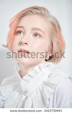 A charming teenage girl with a short haircut and blonde hair with orange streaks poses in a white blouse on a white studio background. Adolescence. Beauty, style and fashion.