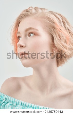 A cute blonde teenage girl with a short haircut in a summer sundress poses against a white wall. Delicate spring-summer look. Beauty, cosmetics.