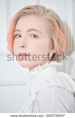 A cute teenage girl with a short haircut and blonde hair with orange streaks poses in a white blouse on a white studio background. Adolescence. Beauty, style and fashion.