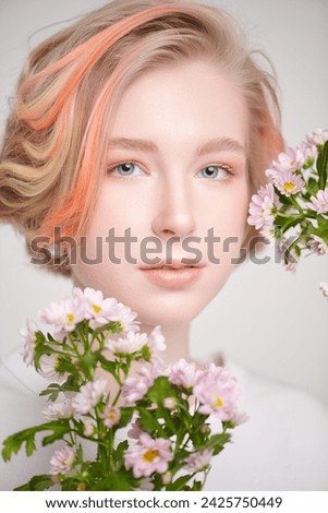 A cute blonde teenage girl with a short haircut in a summer sundress  poses with flowers. Delicate spring-summer look. Beauty, cosmetics.