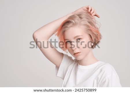Youth style. A cute teenage girl with a short haircut and blonde hair with orange streaks poses in a white T-shirt on a white studio background. Adolescence. Beauty and Fashion. Copy space.
