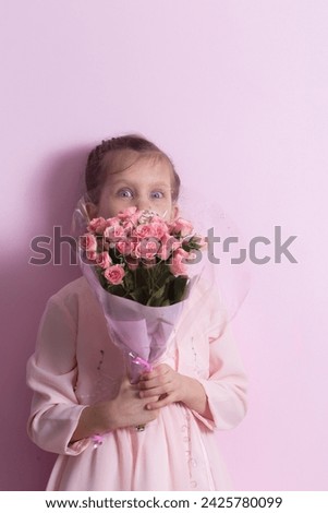 A cute little girl in a pink dress holds a bouquet of pink roses on a pink background