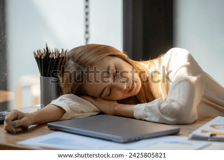 Overworked businesswoman catching a quick nap at her desk in a sunny office.