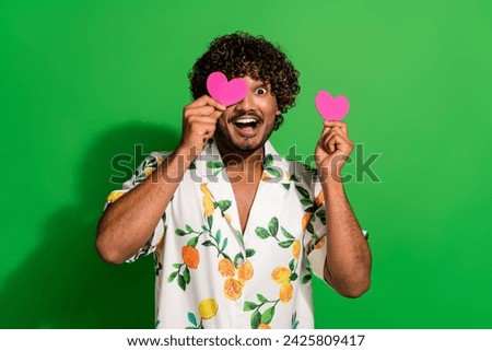 Photo of funky cheerful arabian man wear print shirt pink heart card cover eye isolated green color background